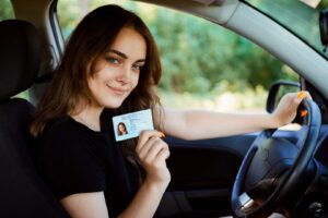 young girl with beautiful smile sitting in car showing driving license to the camera